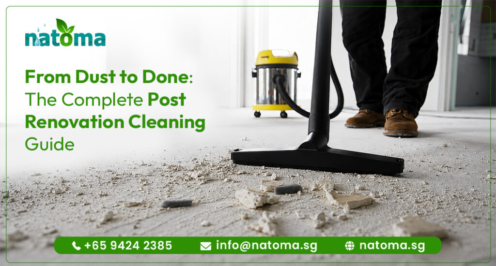 A close-up, low-angle shot of a black vacuum floor attachment cleaning up fine white construction dust and debris from a concrete floor. In the background, the lower legs of a person wearing black pants and brown work boots are visible, alongside a yellow and metallic wet/dry shop vacuum.
